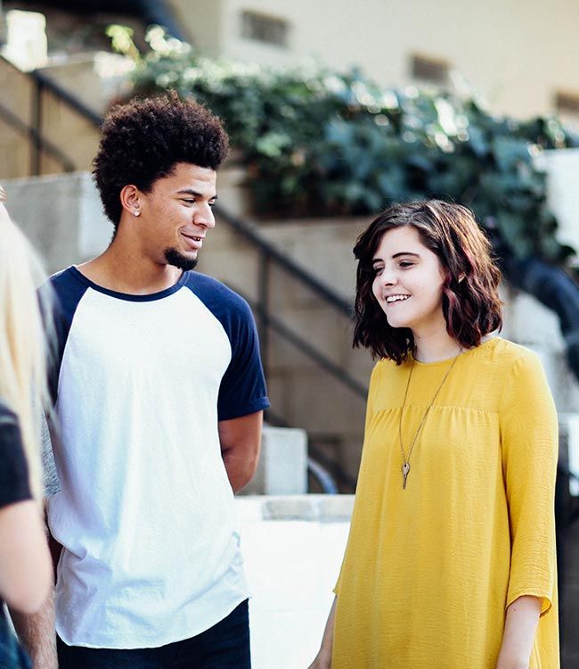 Un homme en maillot de baseball et une femme en robe jaune discutent en extérieur.