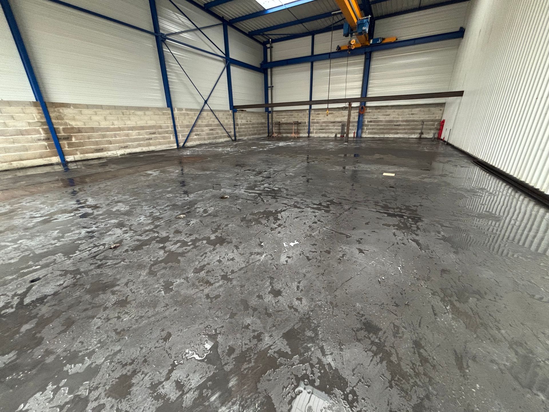 À l'intérieur d'un entrepôt avec un sol humide, des supports visibles et de hauts plafonds.