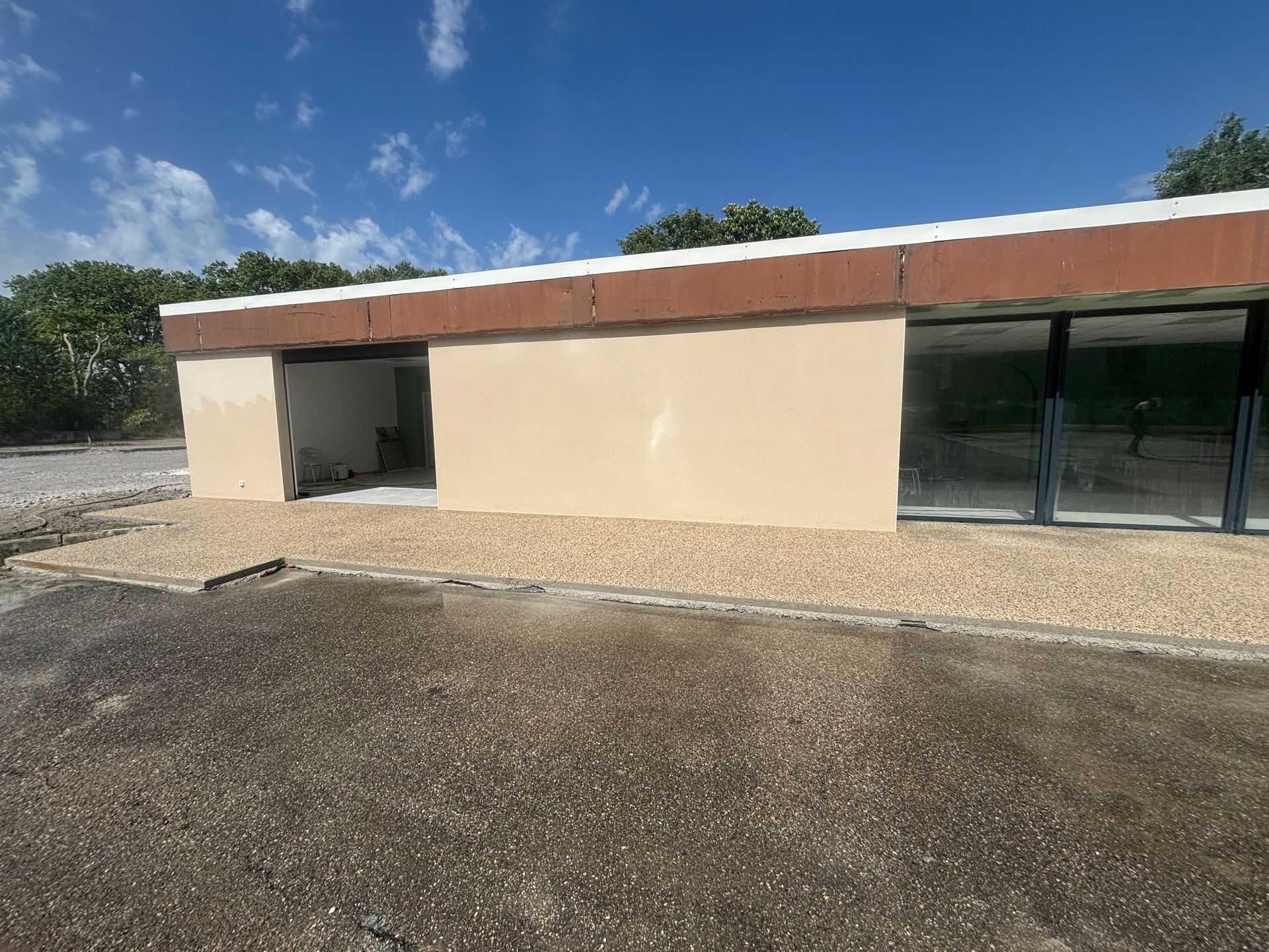 Bâtiment beige avec des garnitures brunes et de grandes fenêtres en verre, se détachant sur un ciel bleu.