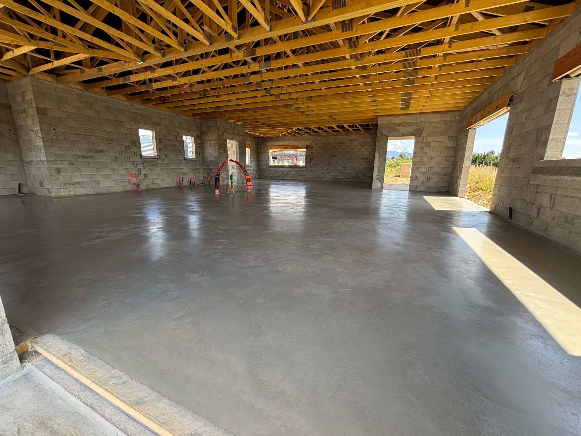 Installation en béton fraîchement coulé dans un bâtiment inachevé avec fermes de toit en bois apparentes et murs en parpaings.