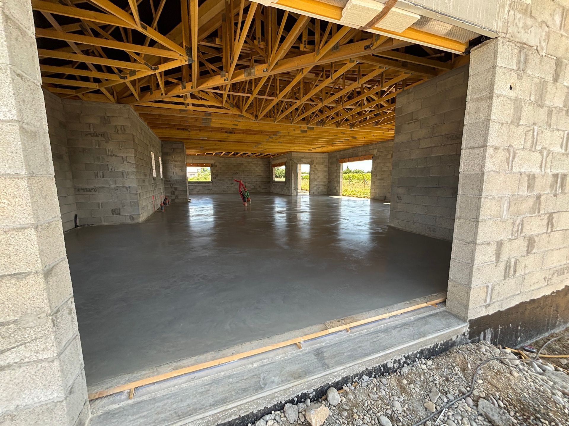 Intérieur de bâtiment inachevé avec un sol en béton, des murs et des poutres en bois apparentes.