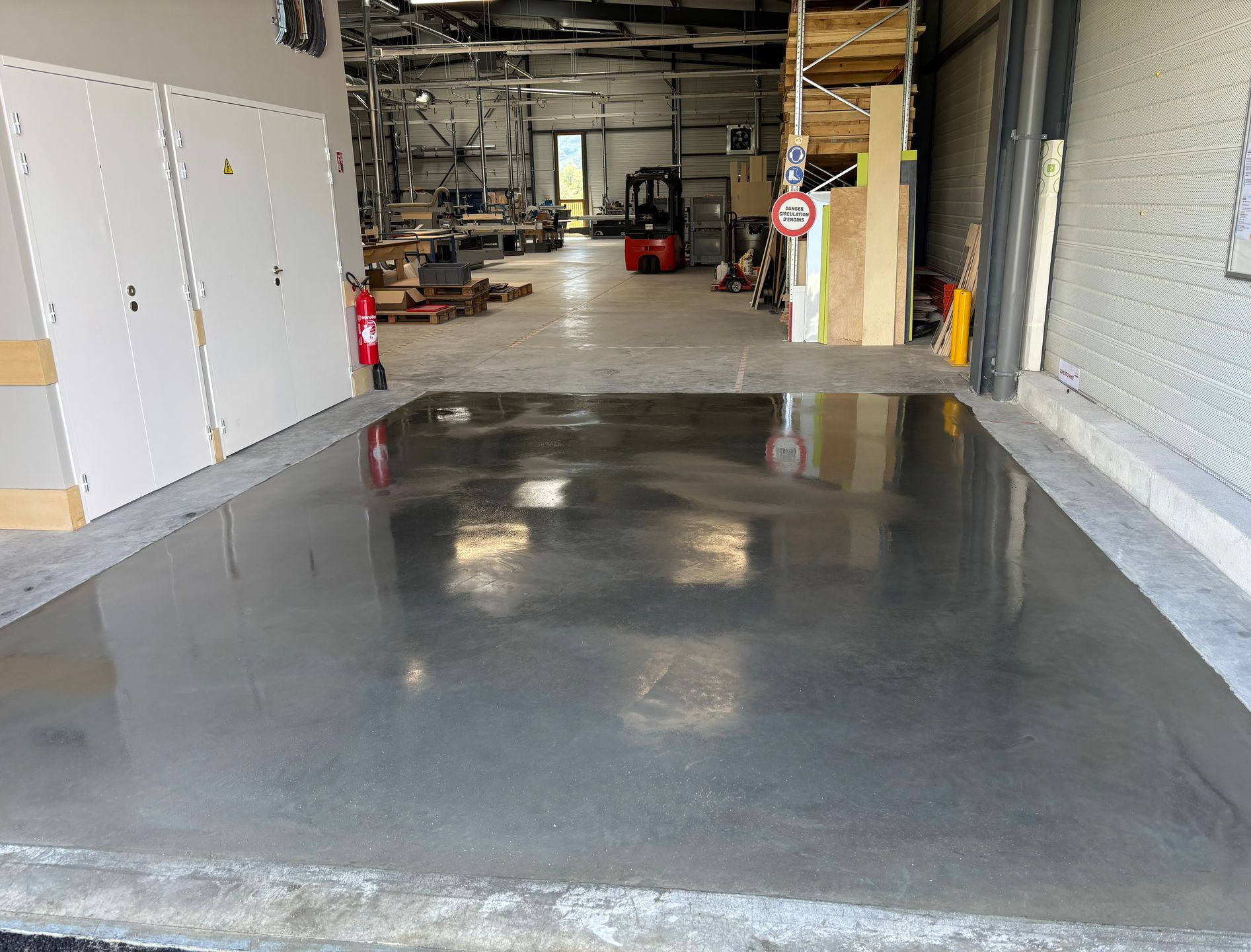 Une rampe en béton gris mène à un entrepôt. Un chariot élévateur et du matériel se trouvent à l'intérieur.