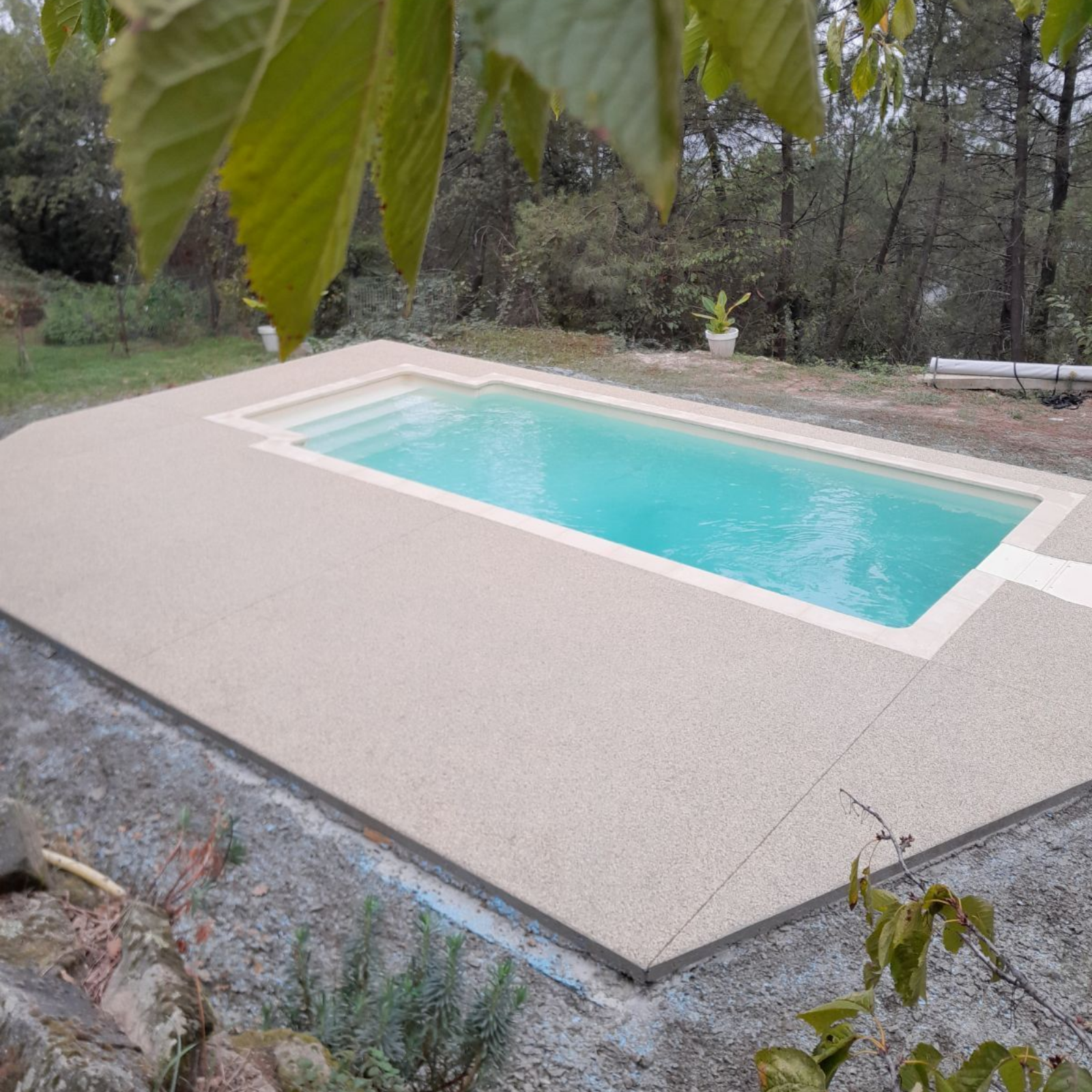 Piscine rectangulaire avec plage en béton et escalier. Extérieur dans un cadre naturel.