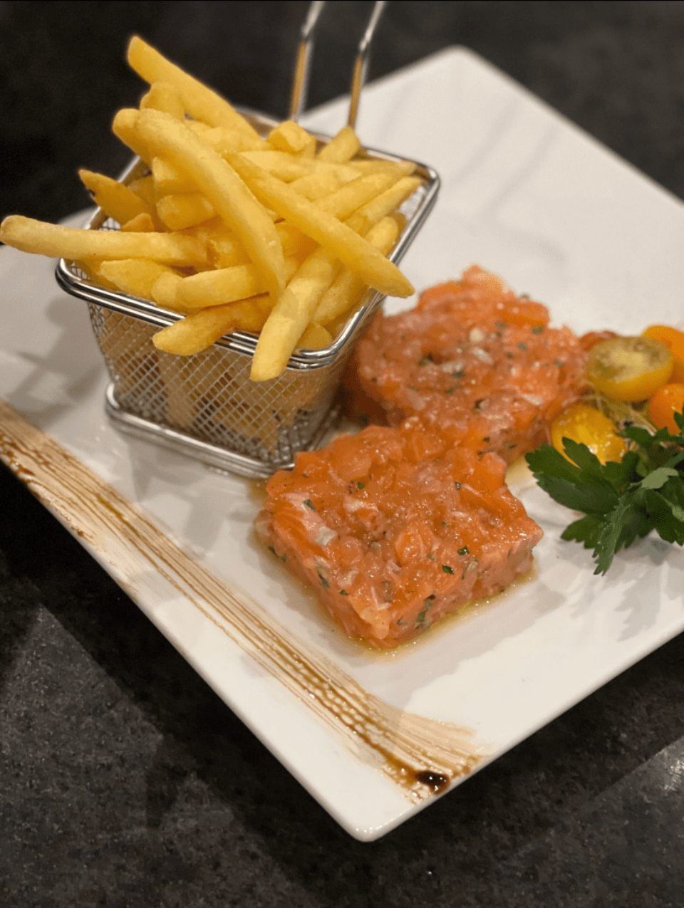 Une assiette blanche garnie de tartare de saumon saumon et de frites
