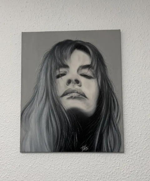 Retrato en blanco y negro de una persona de pelo largo y los ojos cerrados frente a una pared con textura.