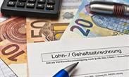 Ein Stift liegt auf einem Blatt Papier neben einem Taschenrechner und Geld.