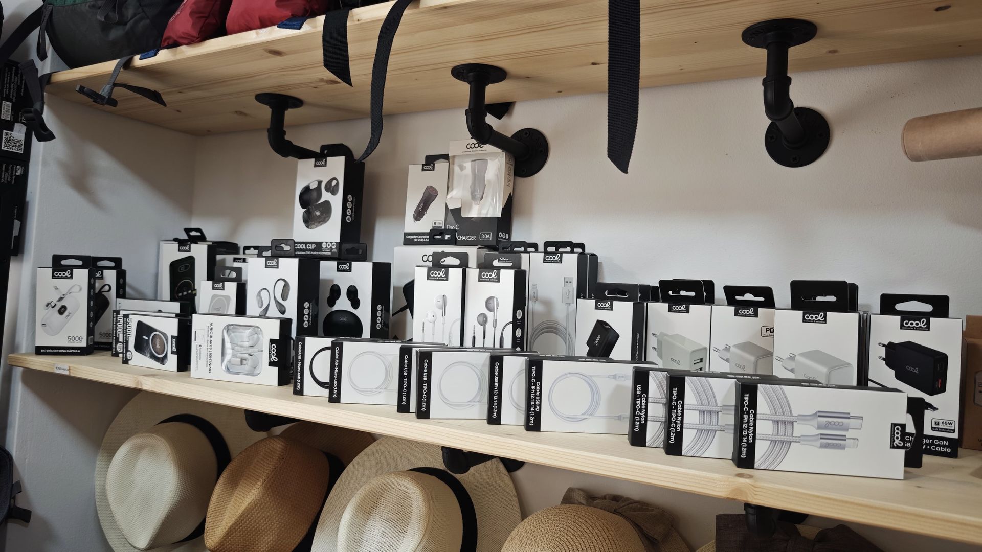 Estanterías con filas de productos en cajas blancas y negras en un expositor de tienda, con sombreros debajo.