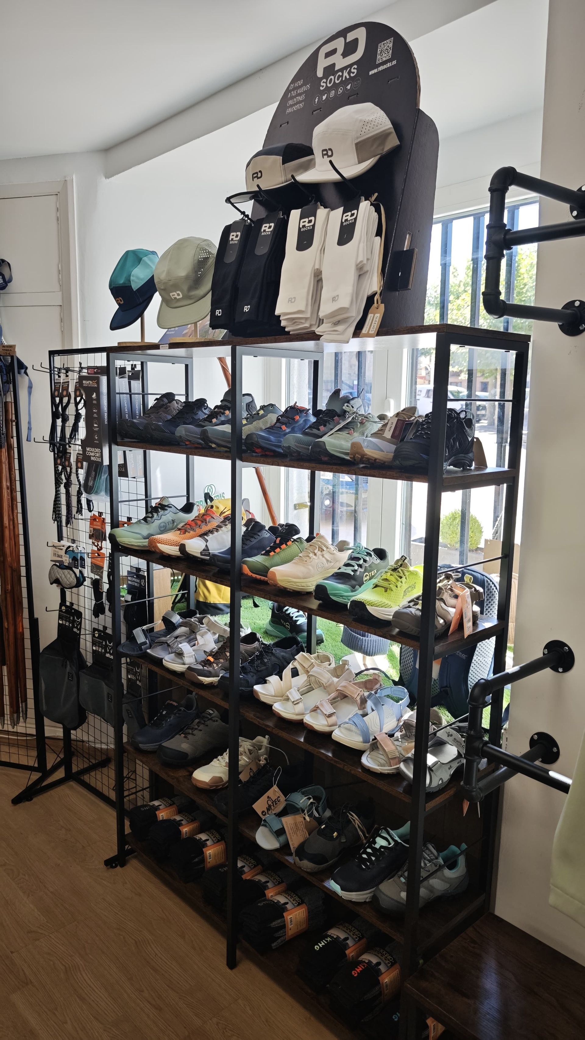 Estanterías de metal negro llenas de distintos zapatos y botas en el recibidor de una casa, con sombreros y mochilas encima.