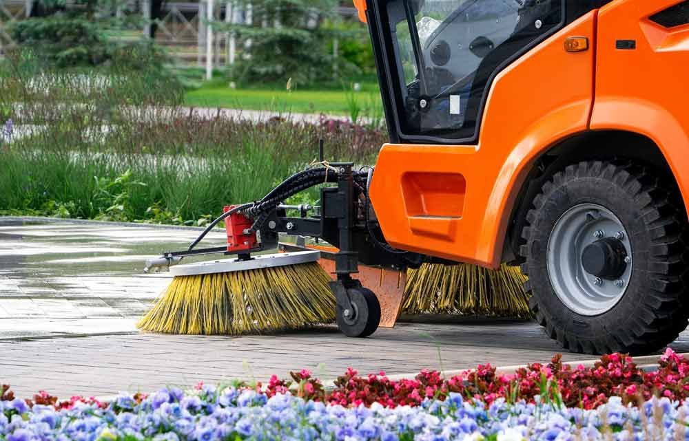 ein orangefarbenes Auto mit einer Bürste , die einen Bürgersteig säubert .