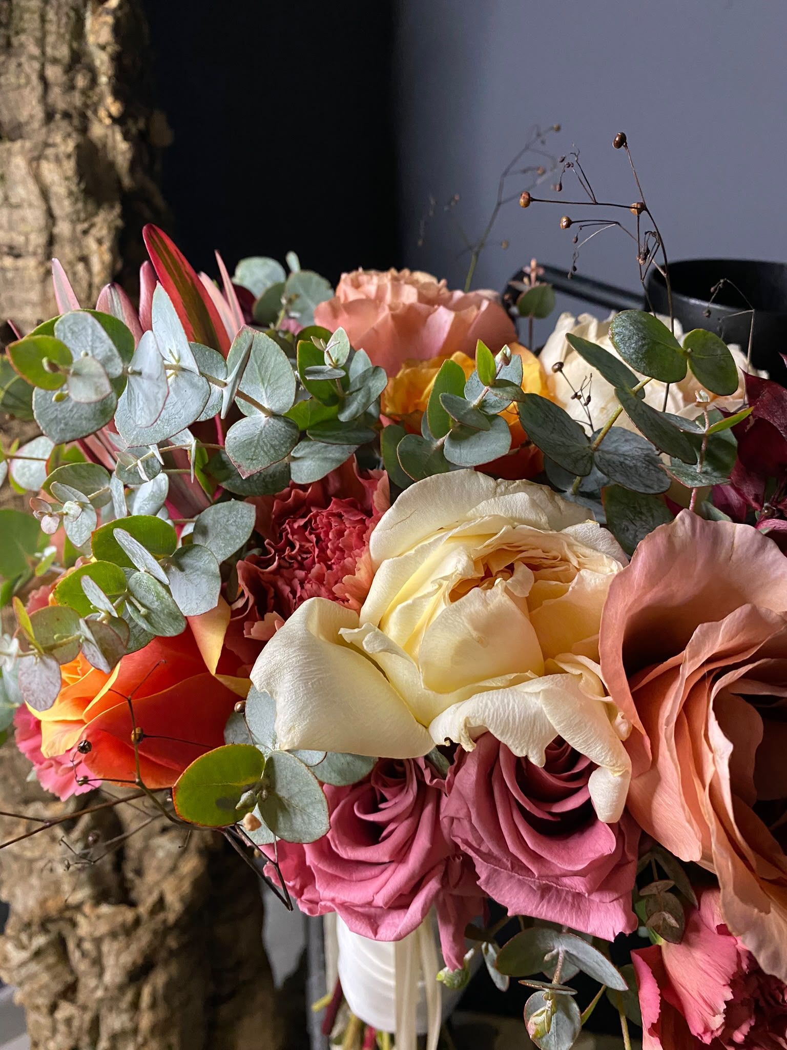 Ramo de flores rosas, crema y rojas con follaje de eucalipto sobre un fondo oscuro.