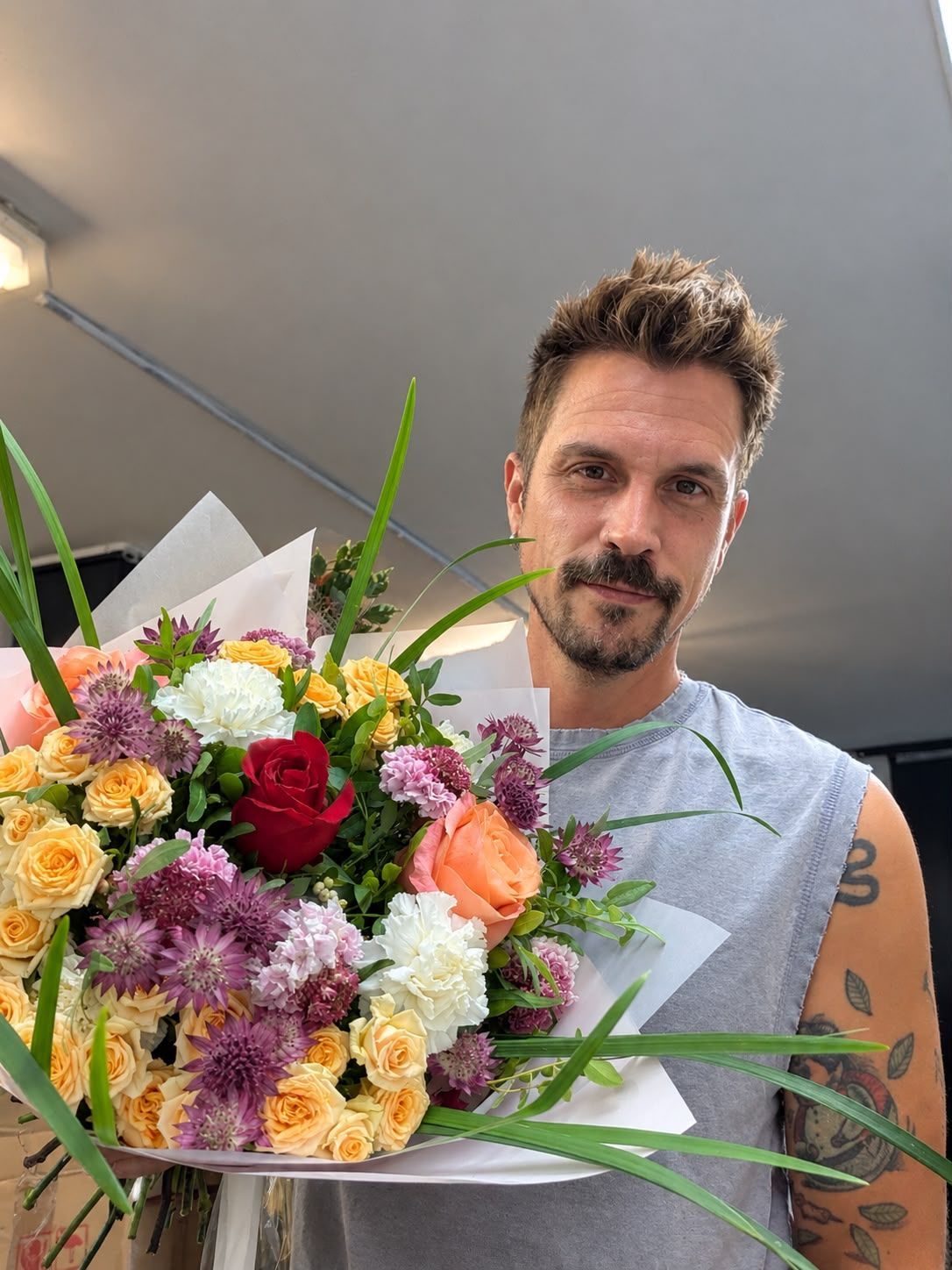 Persona sosteniendo un gran ramo de flores coloridas en el interior de un edificio.