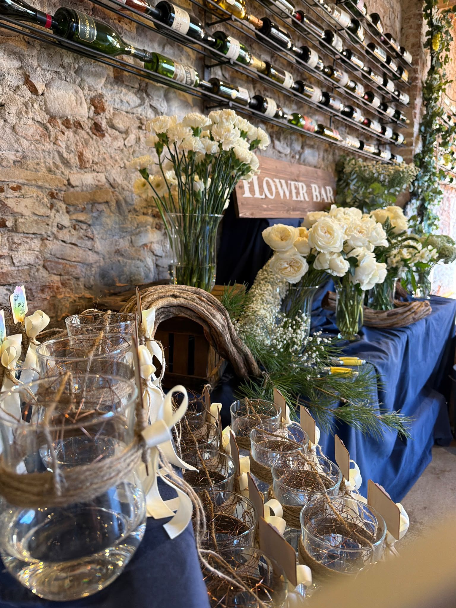 Arreglo floral rústico con flores blancas, botellas de vidrio y un letrero que dice