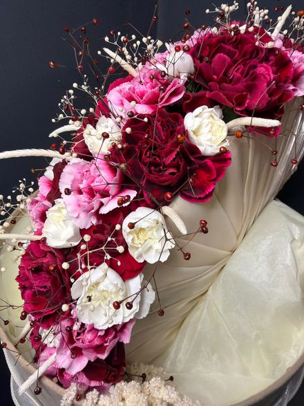 Ramo de flores rosas, burdeos y blancas envuelto en papel color crema sobre un fondo oscuro.