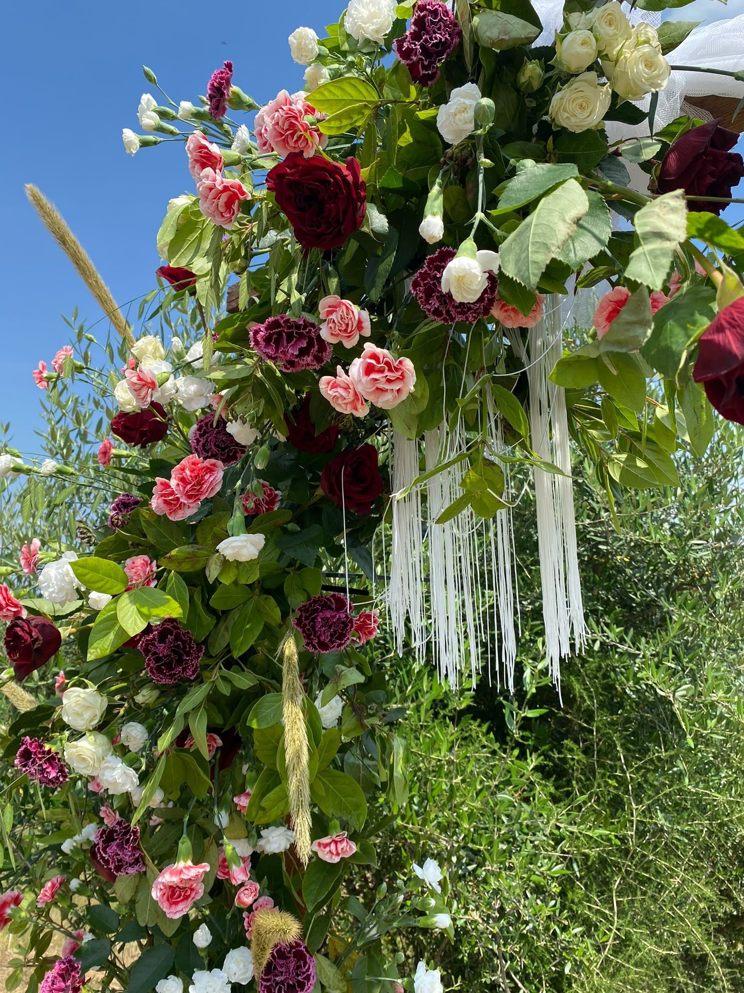 Gran arco floral con flores rosas, rojas, blancas y verdes al aire libre bajo un cielo azul.