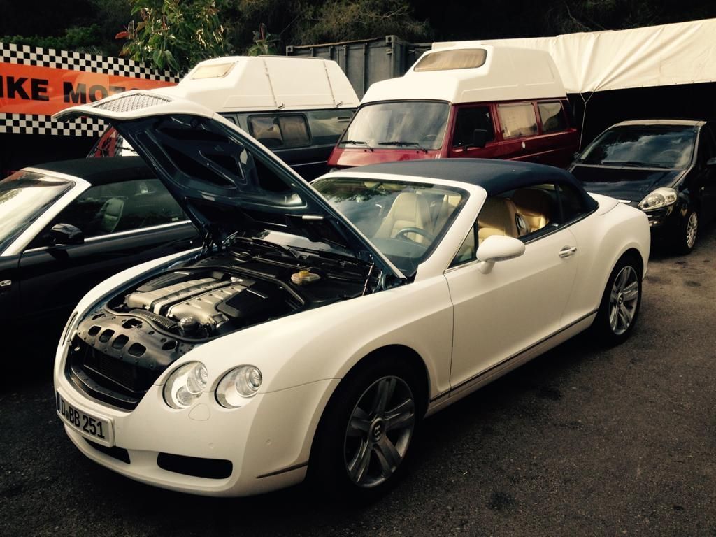 Un automóvil convertible blanco con el capó levantado está estacionado al costado de la carretera.