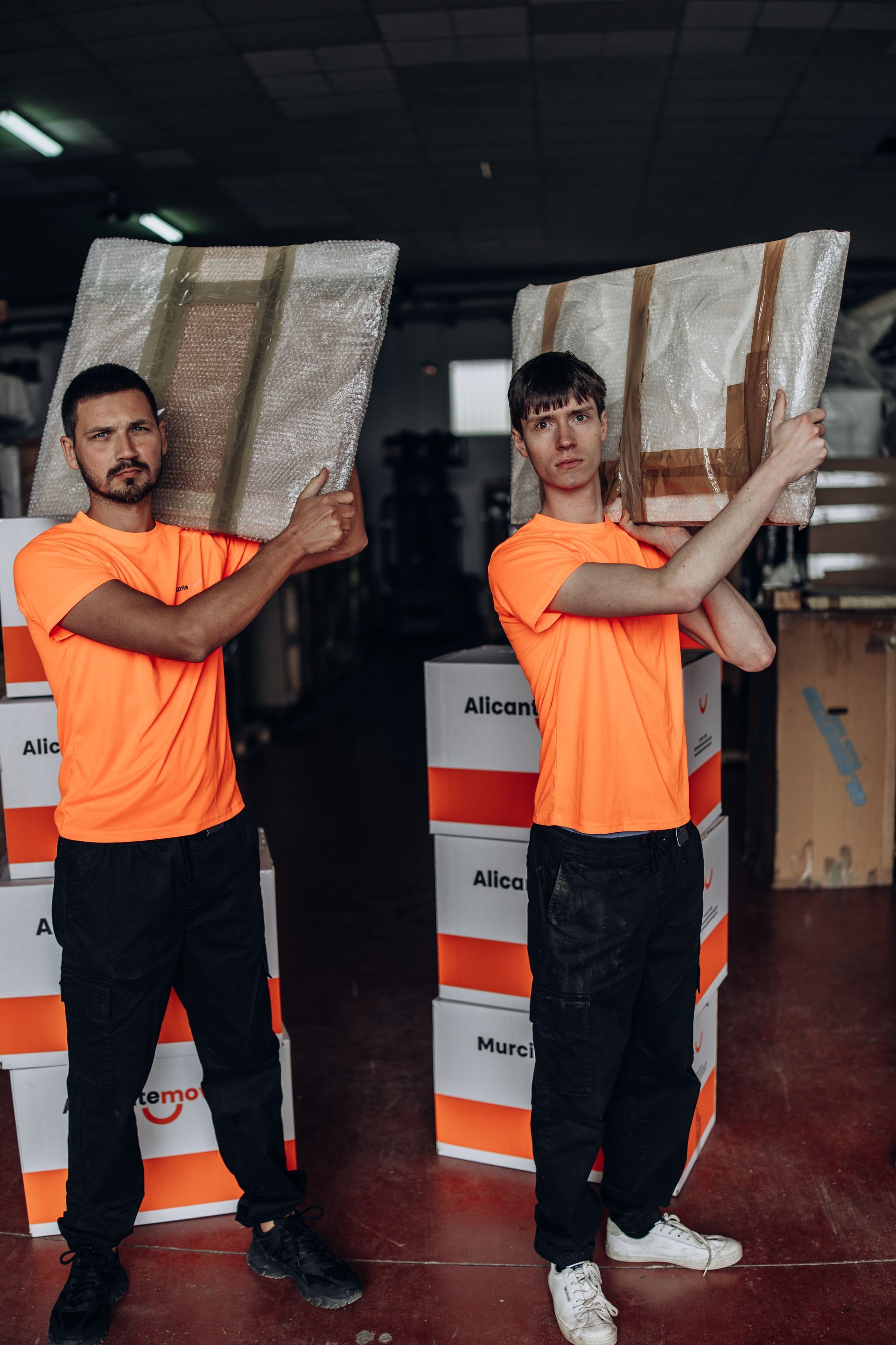 Mujer empacando una caja, colocando plástico de burbujas alrededor de un artículo decorativo, hombre empacando en el fondo.