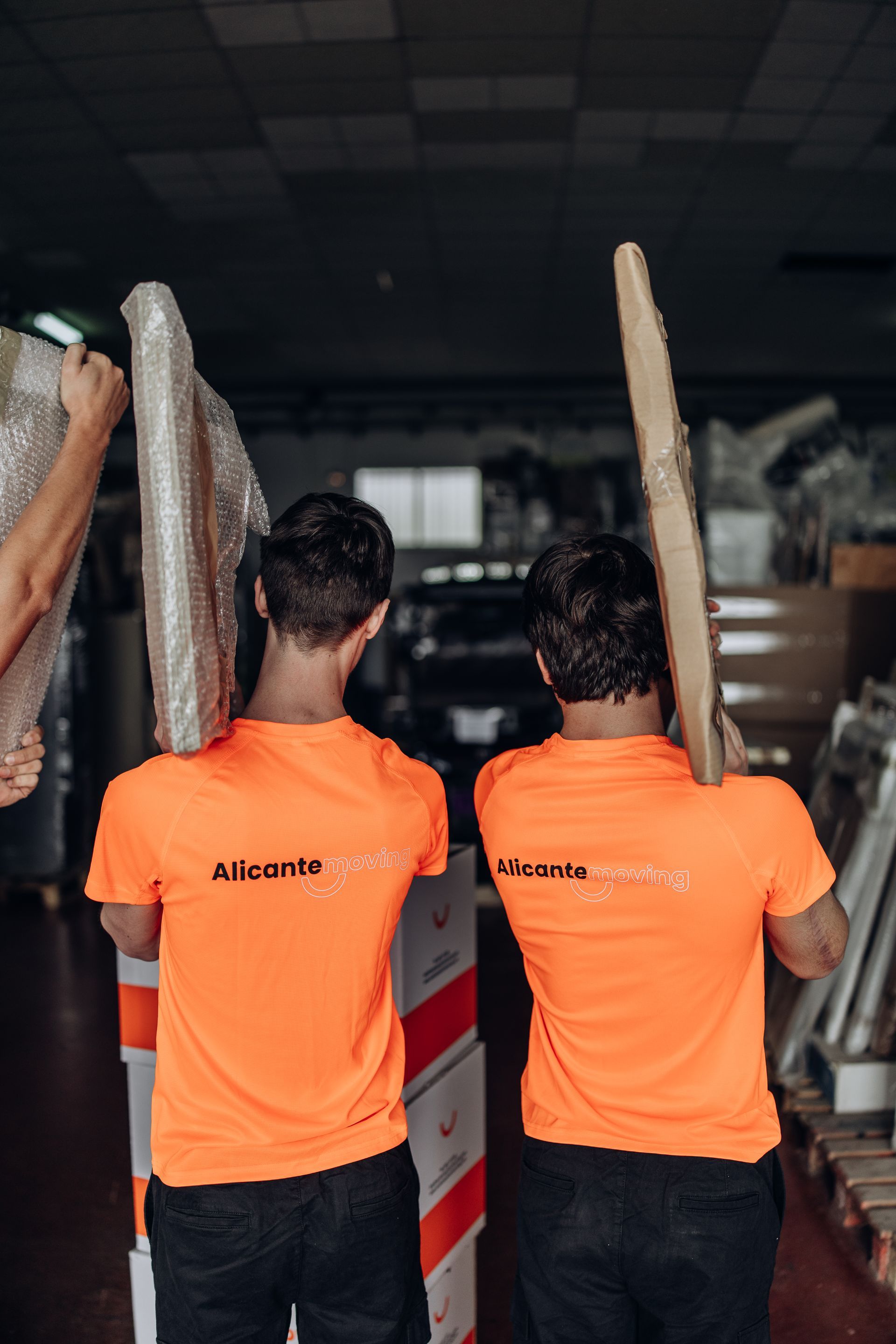 Dos trabajadores de mudanzas transportan artículos a una habitación vacía y luminosa con grandes ventanales.