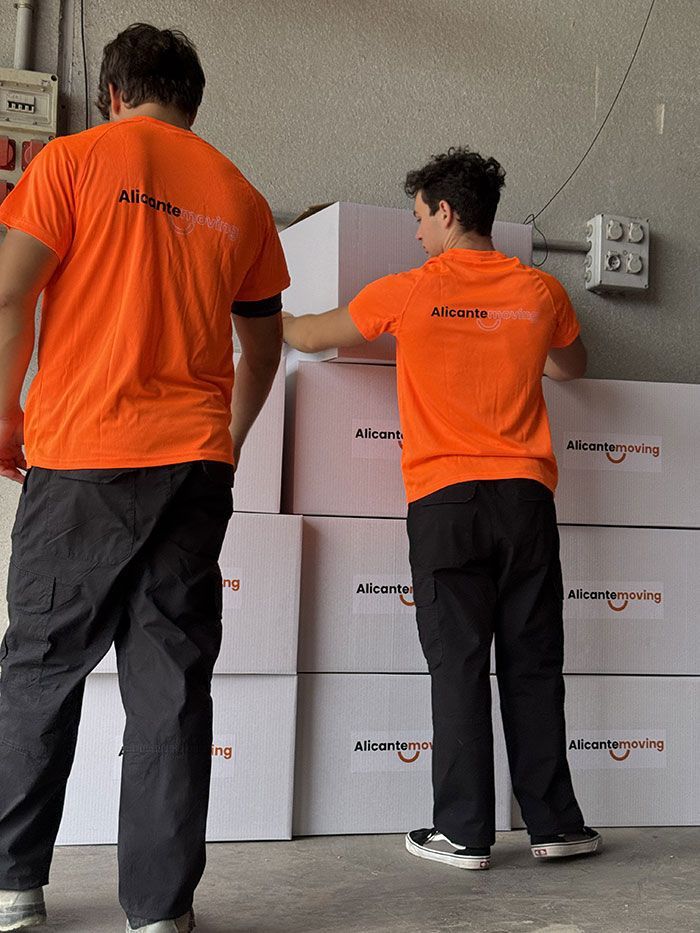 Mujer empacando una caja, colocando plástico de burbujas alrededor de un artículo decorativo, hombre empacando en el fondo.