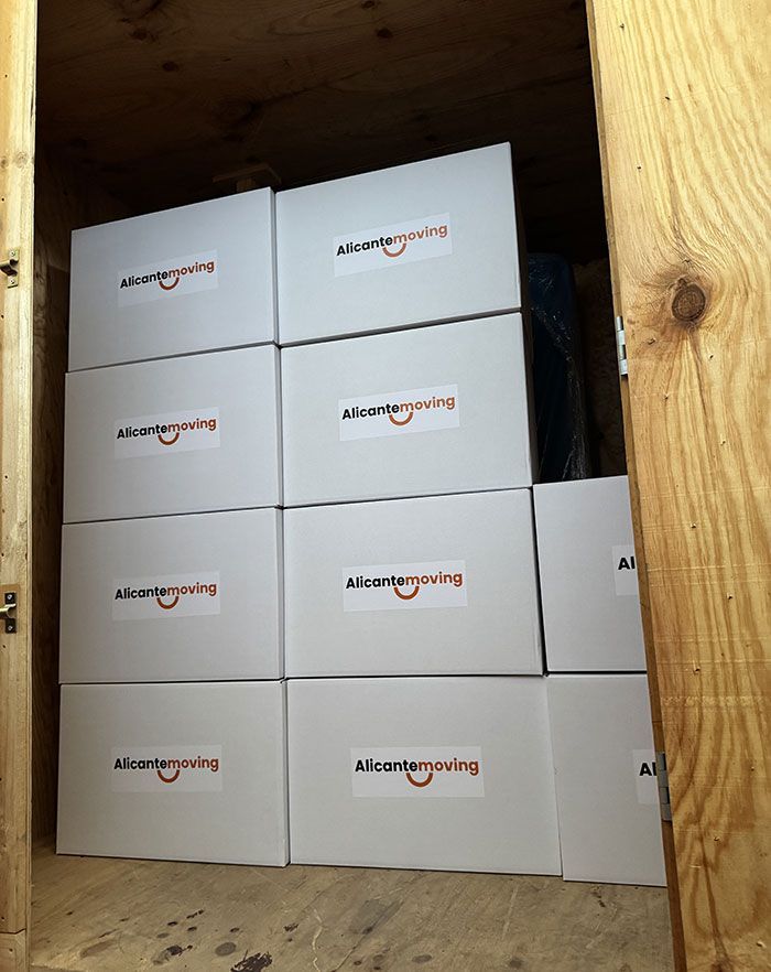 Una habitación llena de cajas de mudanza, muebles y materiales de embalaje. La luz entra a raudales por la ventana.