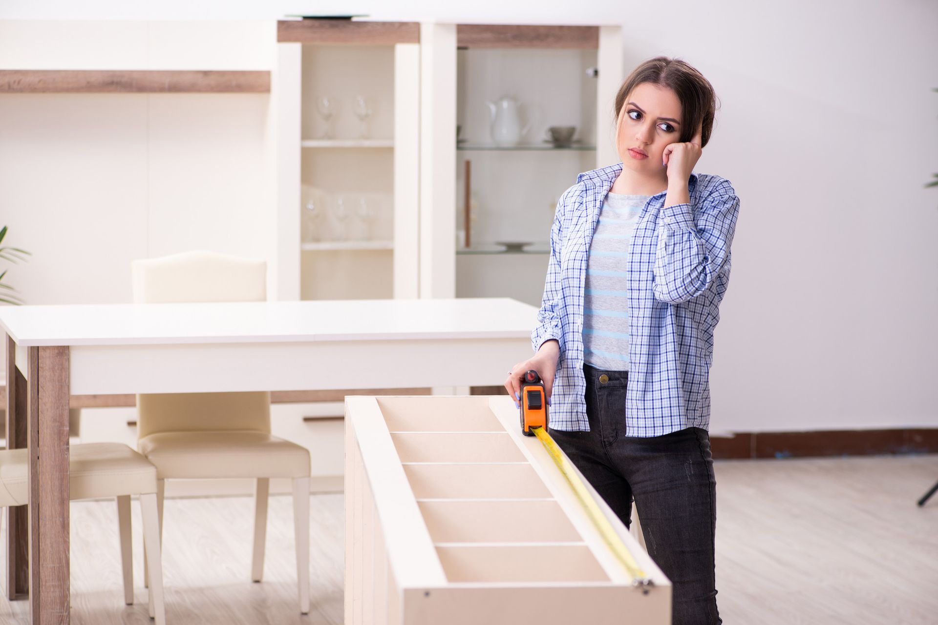 Mujer midiendo muebles, con aspecto pensativo en una habitación llena de luz.