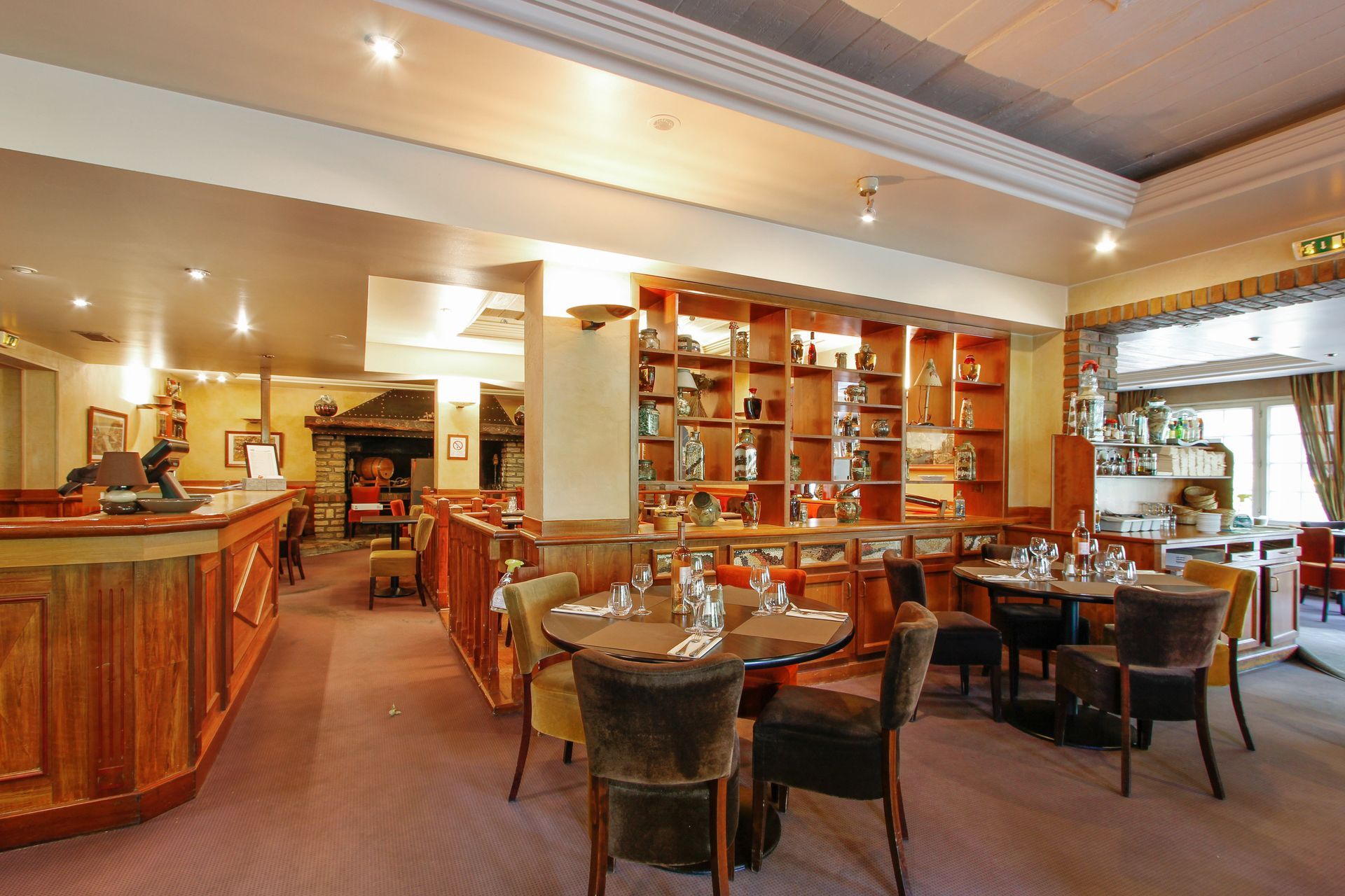 Une salle à manger avec des tables et des chaises en bois foncé, un comptoir de service et une étagère d'exposition éclairée.