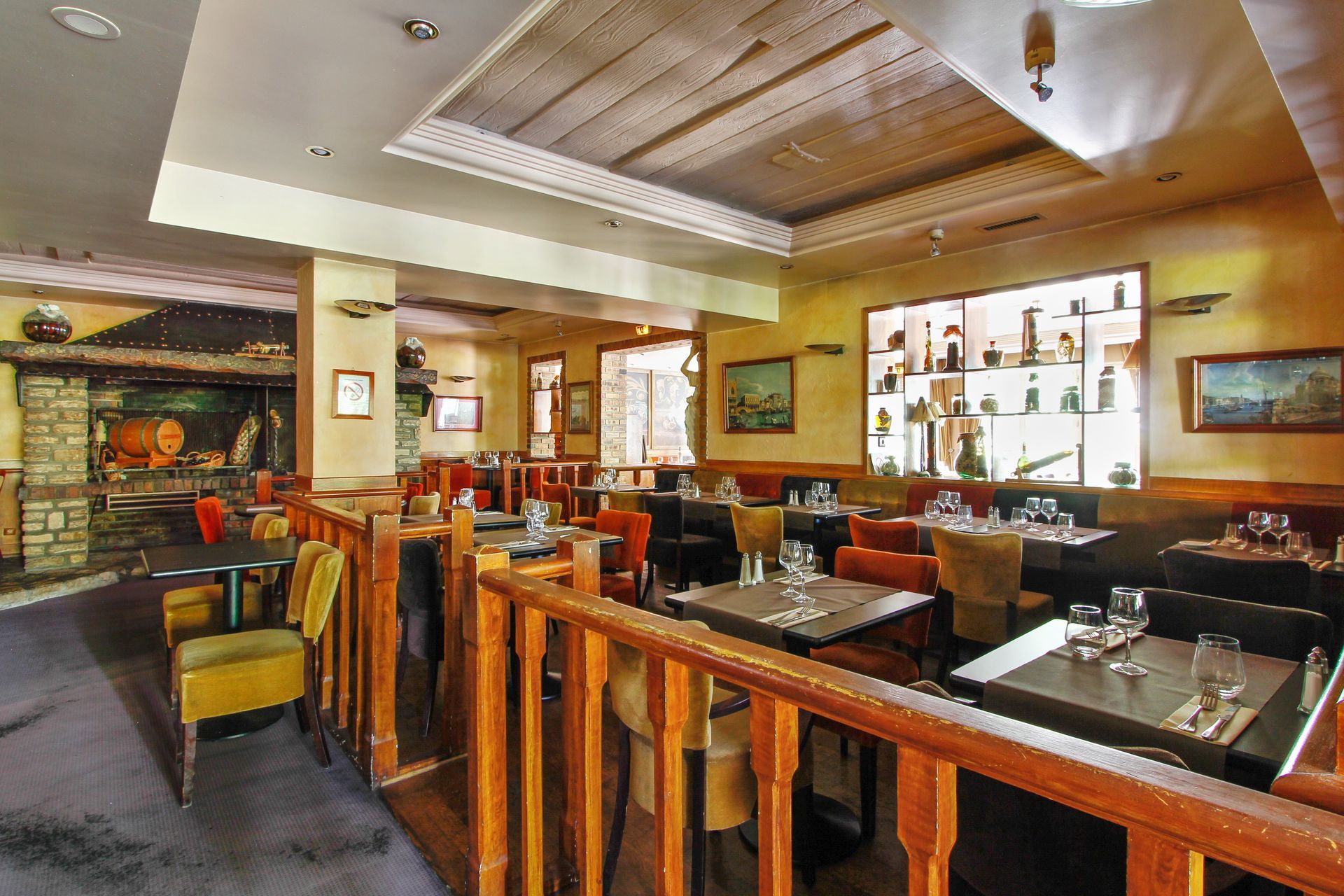 Un intérieur de restaurant rustique et chaleureux, avec des meubles en bois, une cheminée et un éclairage tamisé, et des tables dressées pour le repas.