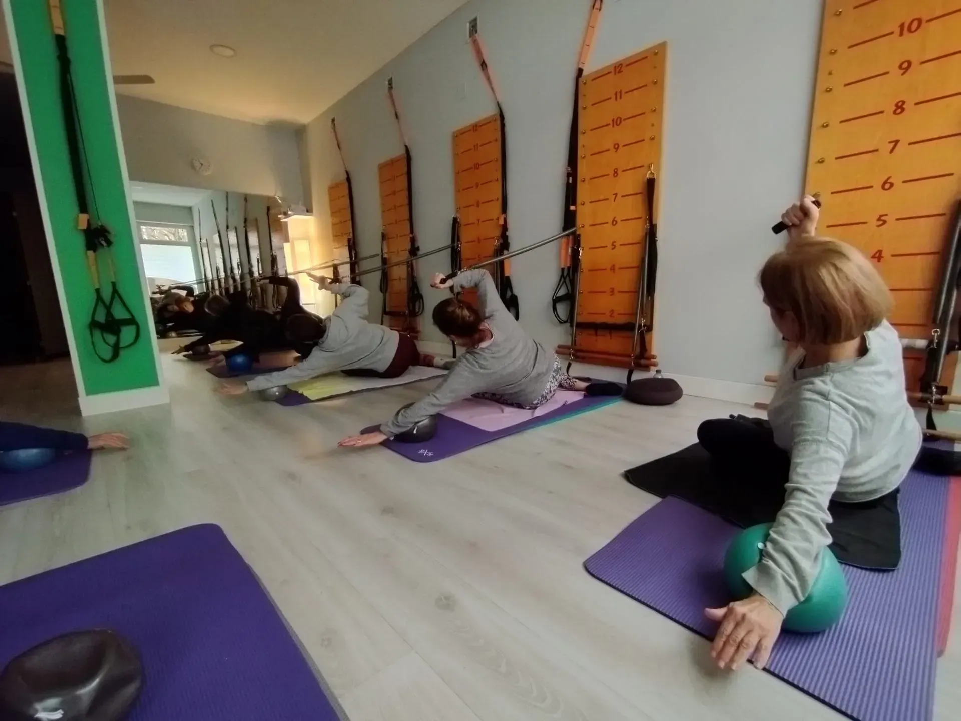 Personas ejercitándose con aparatos en un estudio. El instructor con sus clientes sobre colchonetas.