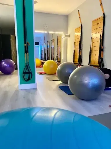 Interior del estudio de pilates: pelotas de ejercicio, reformers, pared verde con correas, espejos.