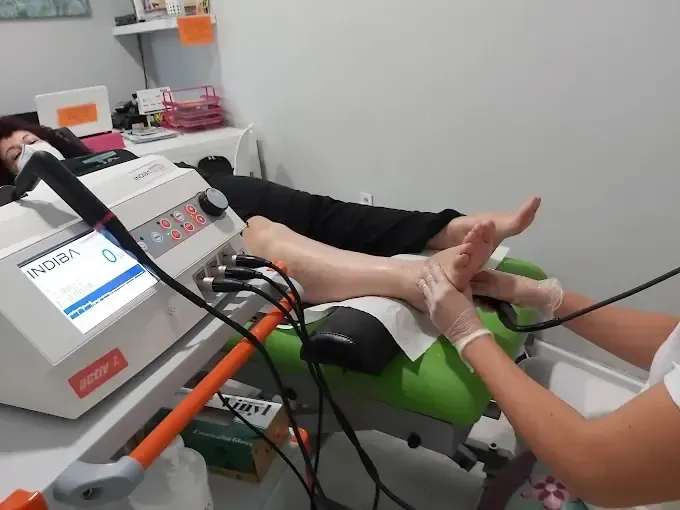 Una persona recibe terapia de pies en una clínica, con una máquina y un terapeuta que usa sus manos.