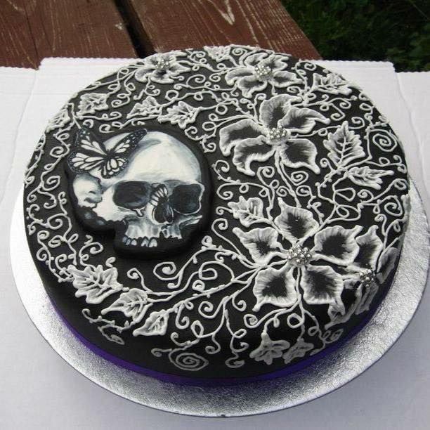 Torta nera con decorazione di glassa bianca a forma di teschio e fiori, su un vassoio d'argento.