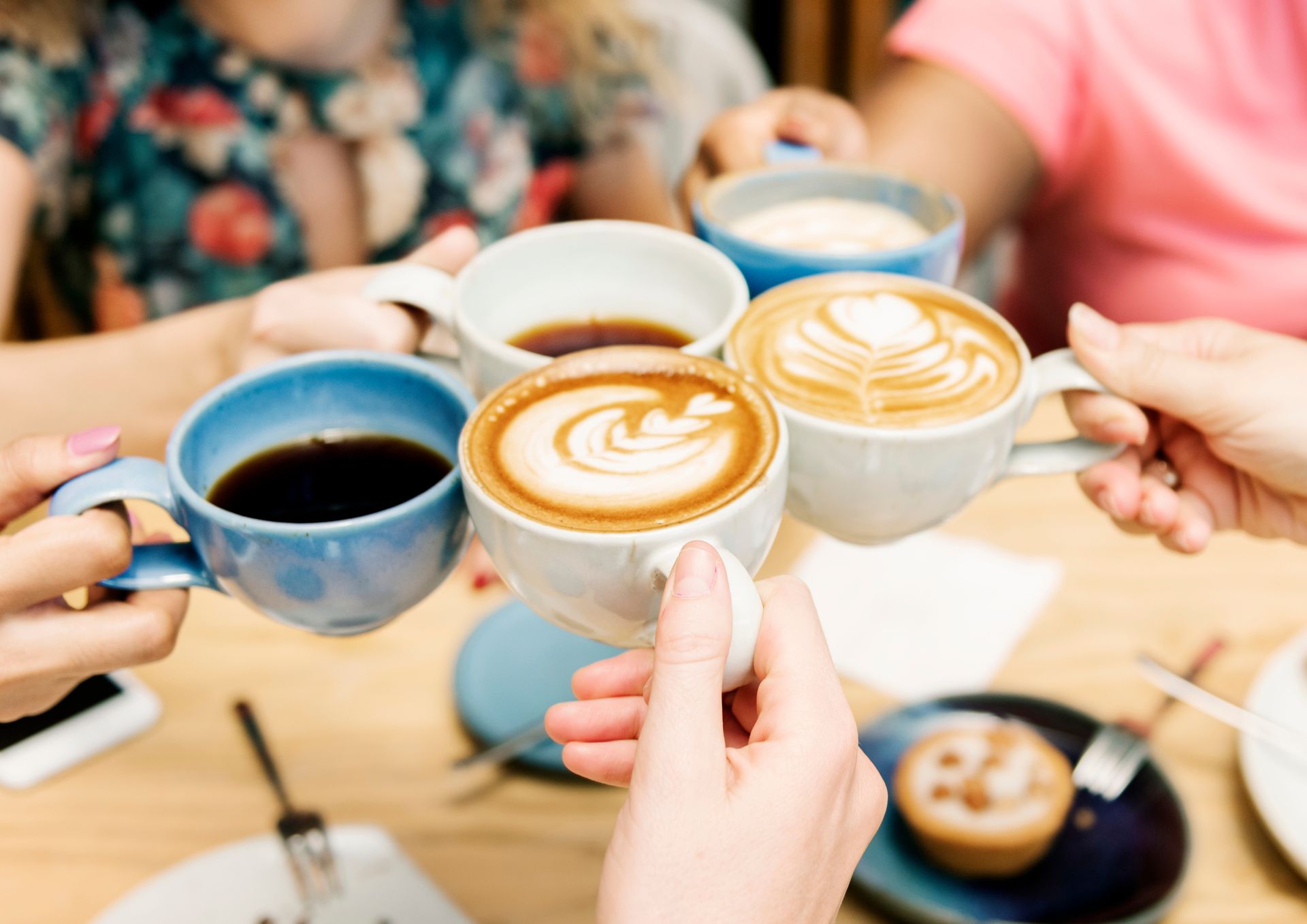 Des mains tenant des tasses à café bleues et blanches dans un café, les boissons étant décorées de latte art.