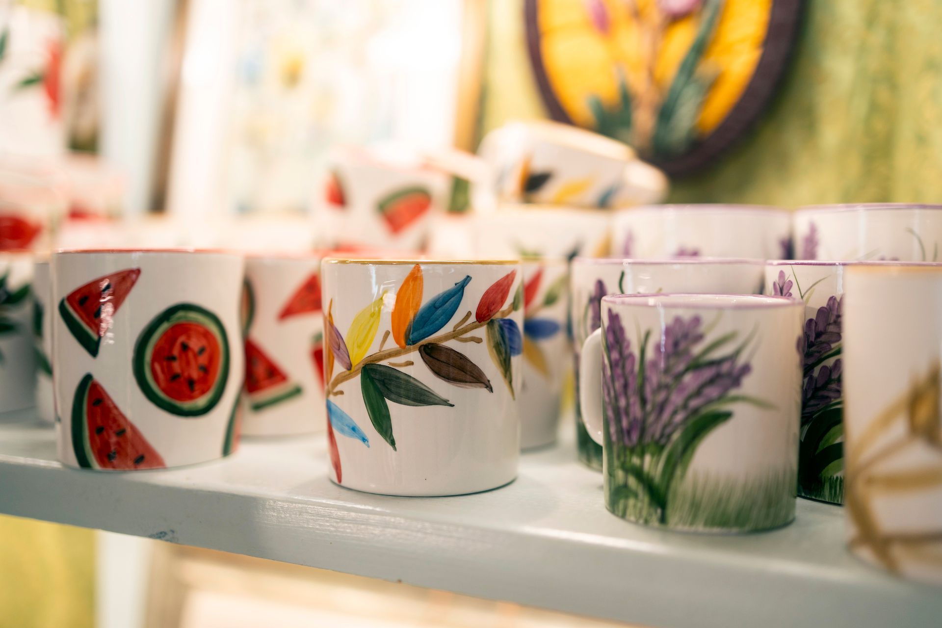 Tasses en céramique peintes à motifs floraux et fruités disposées sur une étagère.