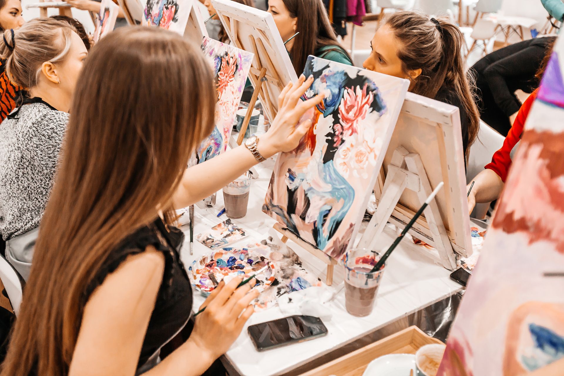 Des artistes peignent sur leurs chevalets dans un atelier animé, avec des pinceaux, des toiles et des tables couvertes de peinture.