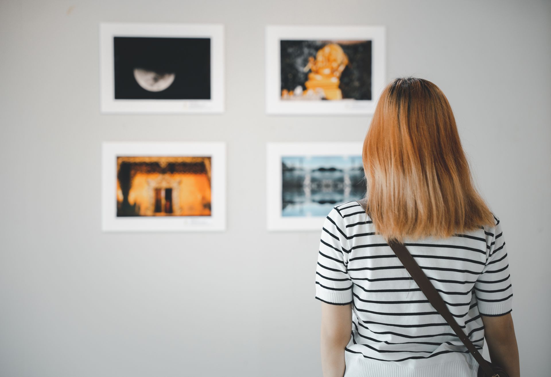 Une personne regarde quatre photos encadrées sur un mur de galerie
