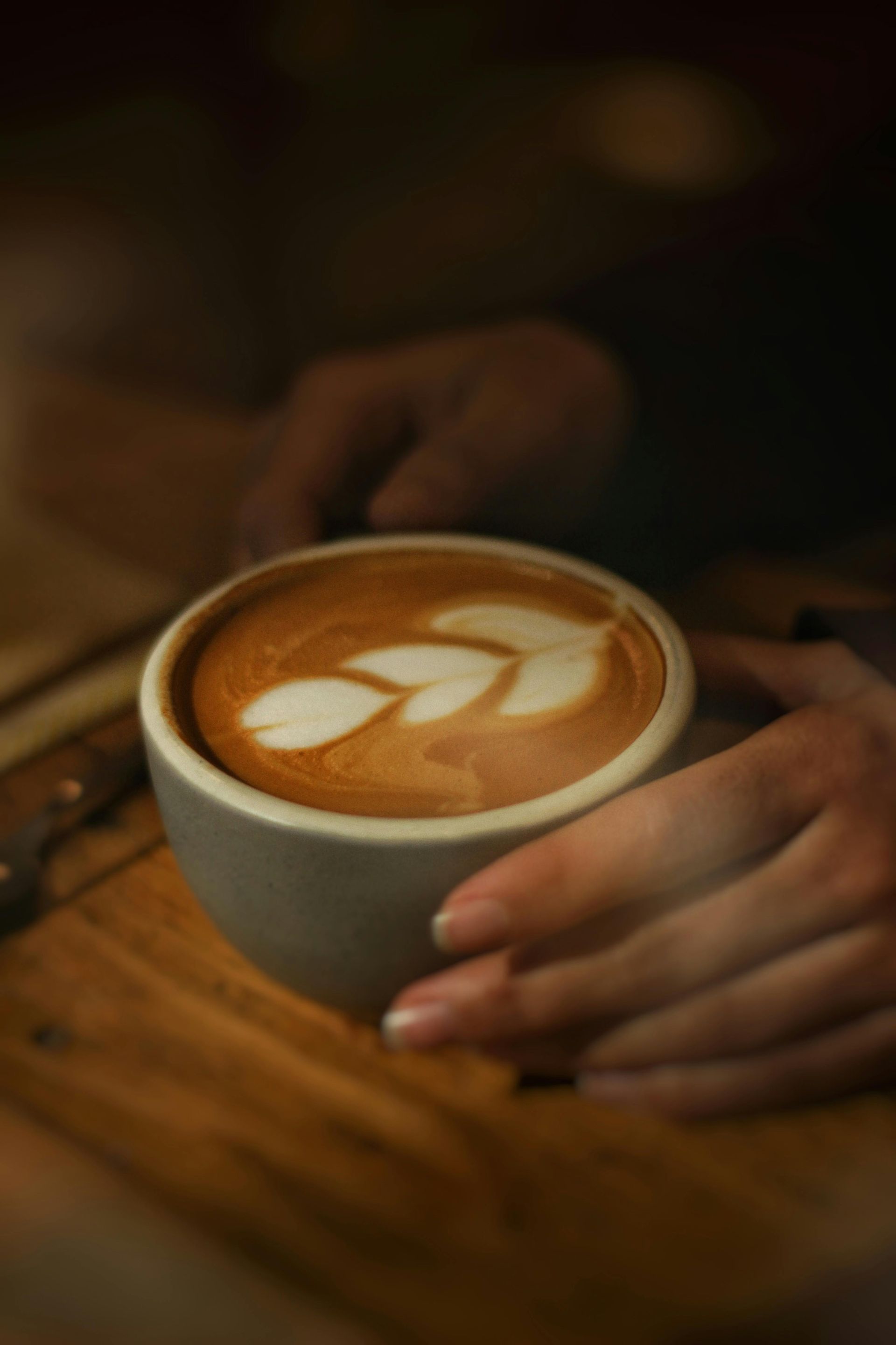 Des mains tenant une tasse de latte décorée de motifs de feuilles sur une table en bois