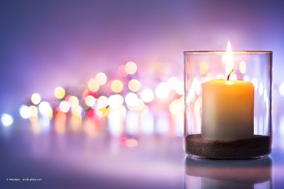 Brennende Kerze in einem Glas, im Hintergrund weitere verschwimmende Kerzen