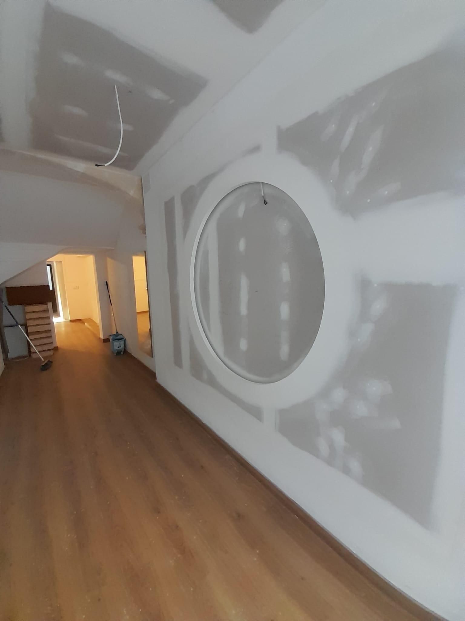 Un pasillo estrecho con suelo de madera clara, paredes blancas y un gran elemento circular empotrado