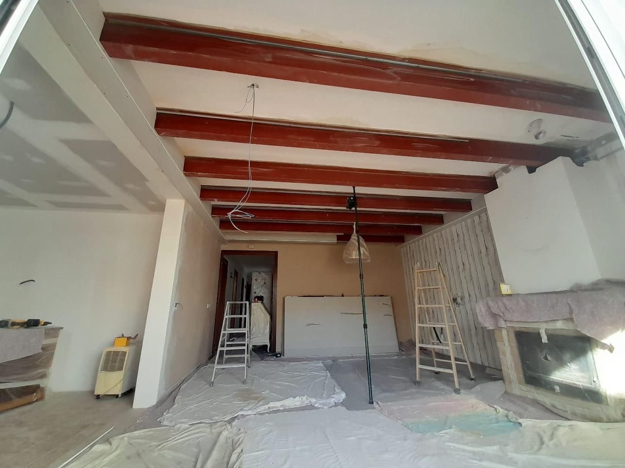 Una habitación en obras con vigas de madera oscuras a la vista en el techo, paredes blancas