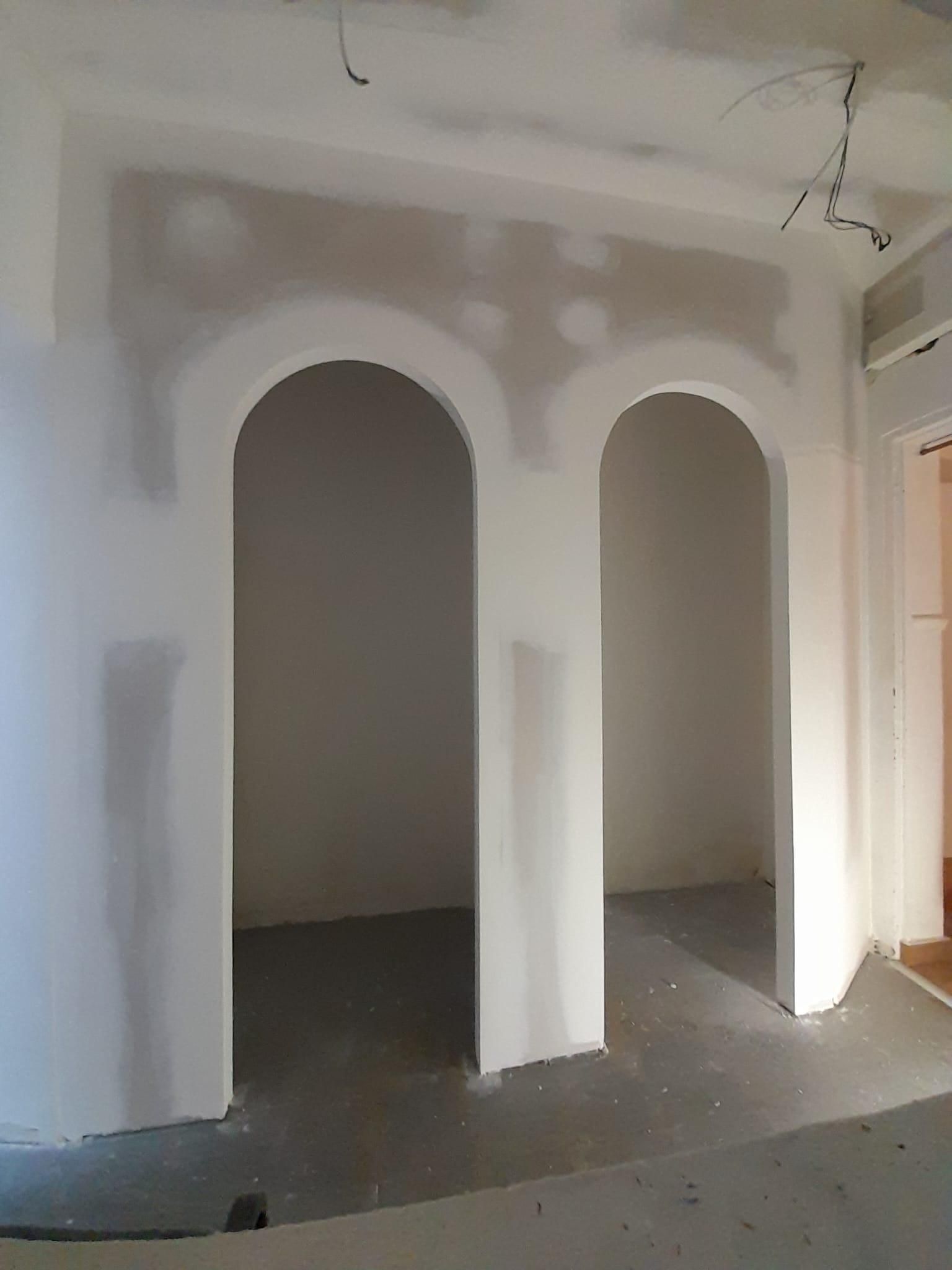 Un muro en construcción con dos puertas arqueadas sin terminar, con parches de paneles de yeso