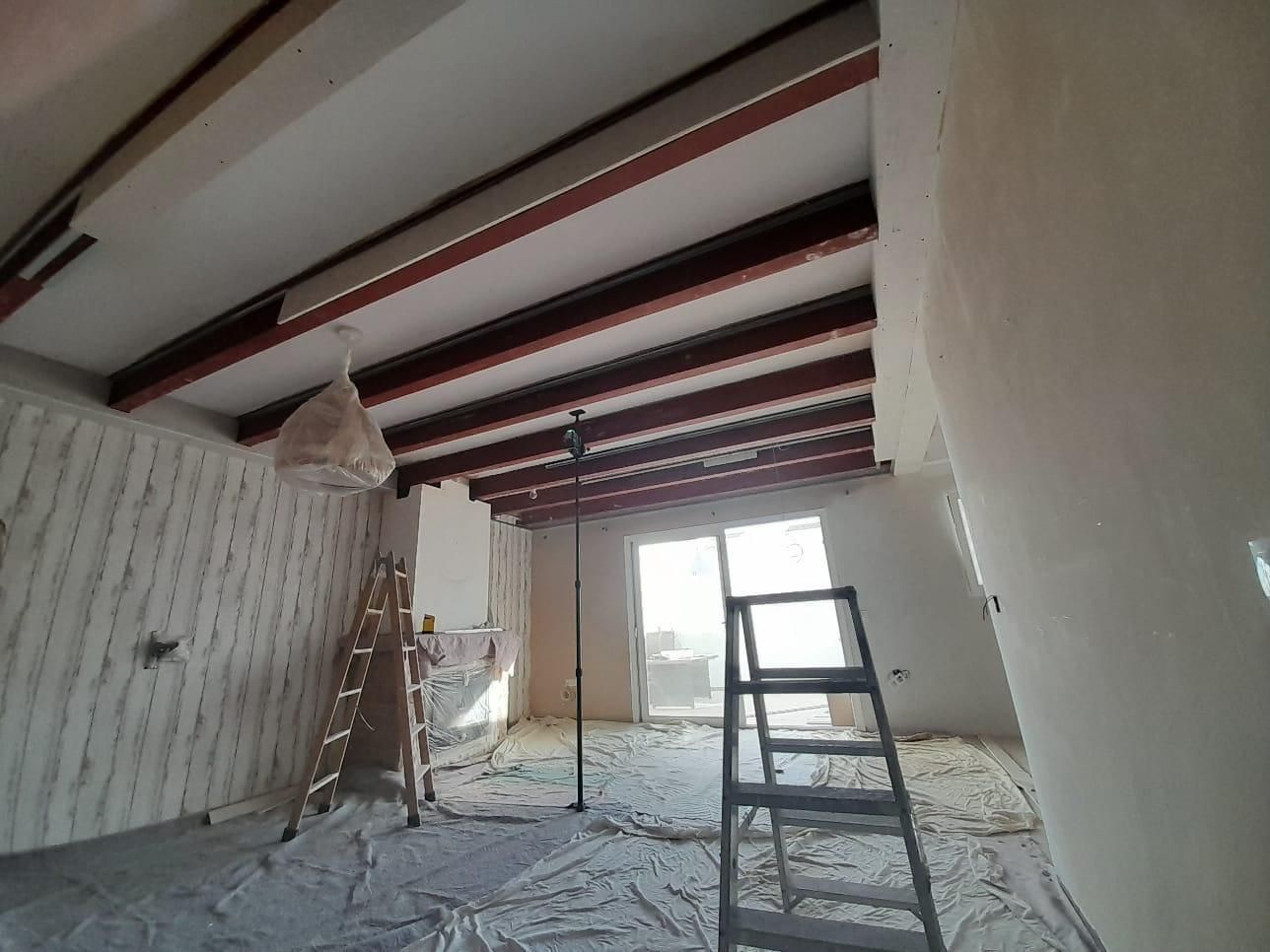 Una habitación interior en obras, con vigas oscuras a la vista en el techo