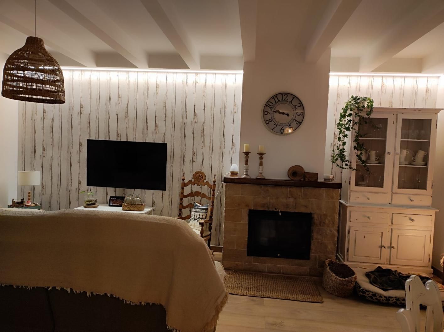 Acogedora sala de estar con chimenea de piedra, techo con vigas de madera, papel pintado texturizado