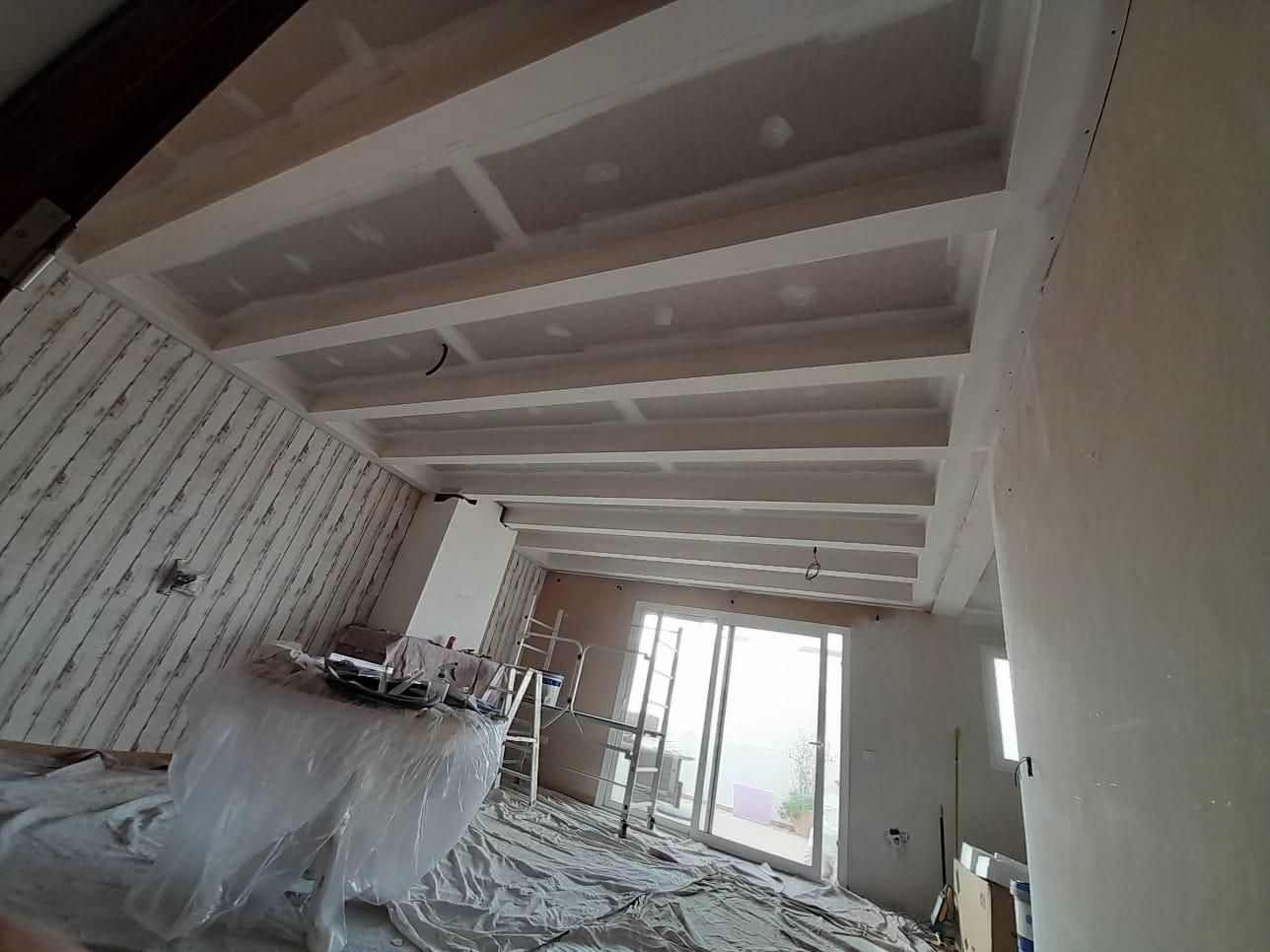Interior de una habitación en proceso de renovación con vigas blancas de techo a la vista, paneles de yeso recién instalados