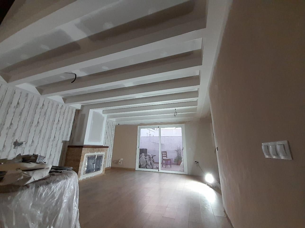 Una habitación de color claro con vigas de madera a la vista en el techo, suelos de madera noble