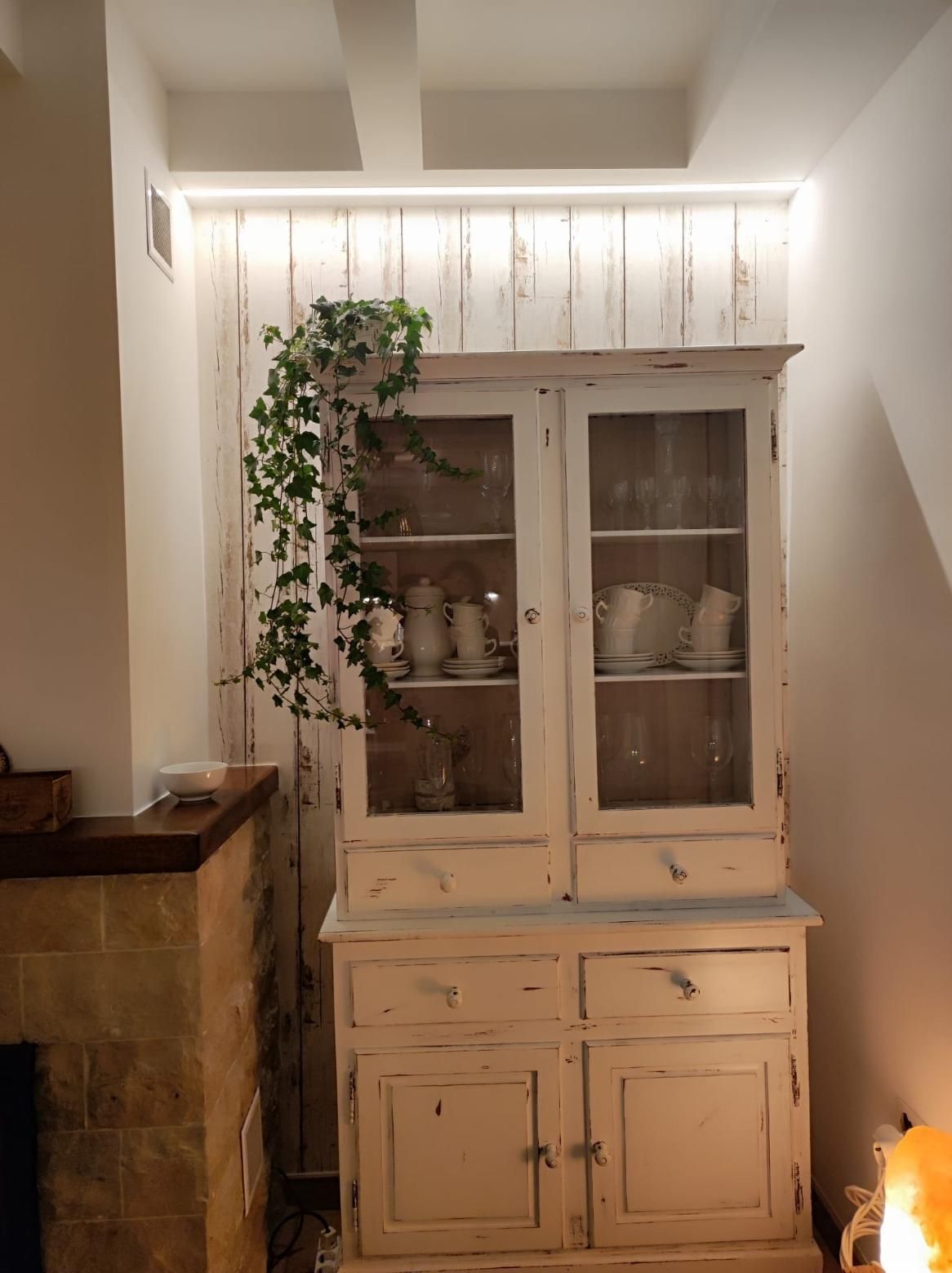 Un aparador rústico de madera blanca, lleno de vajilla, se alza contra una pared revestida con tablones verticales blancos