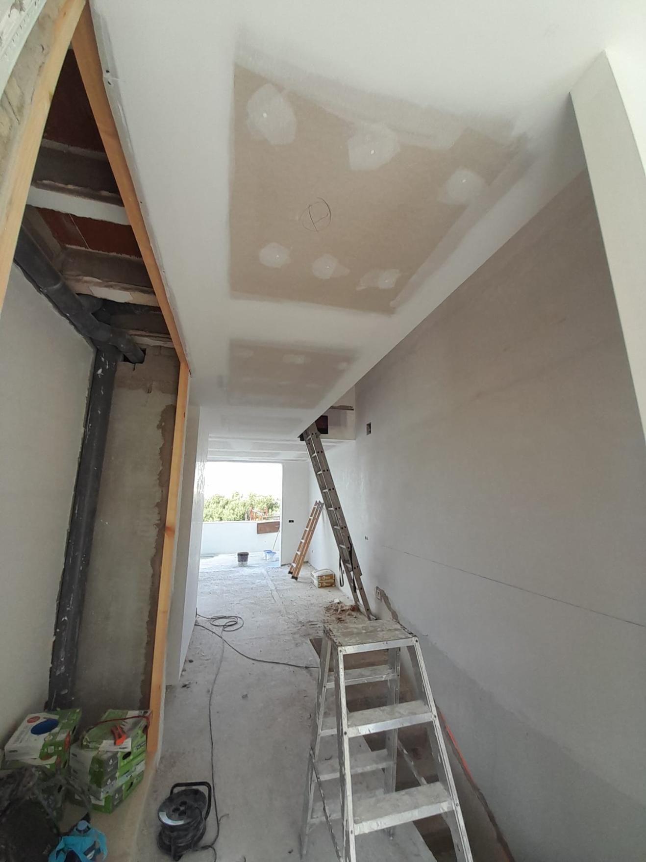 Un pasillo parcialmente renovado con paredes y techo de pladur blanco, una escalera metálica en el centro