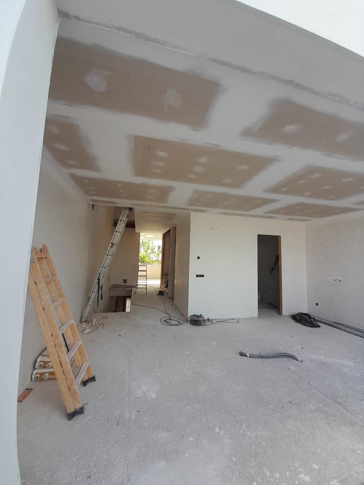 Una habitación sin terminar, en construcción, con una escalera apoyada contra la pared, el techo de pladur