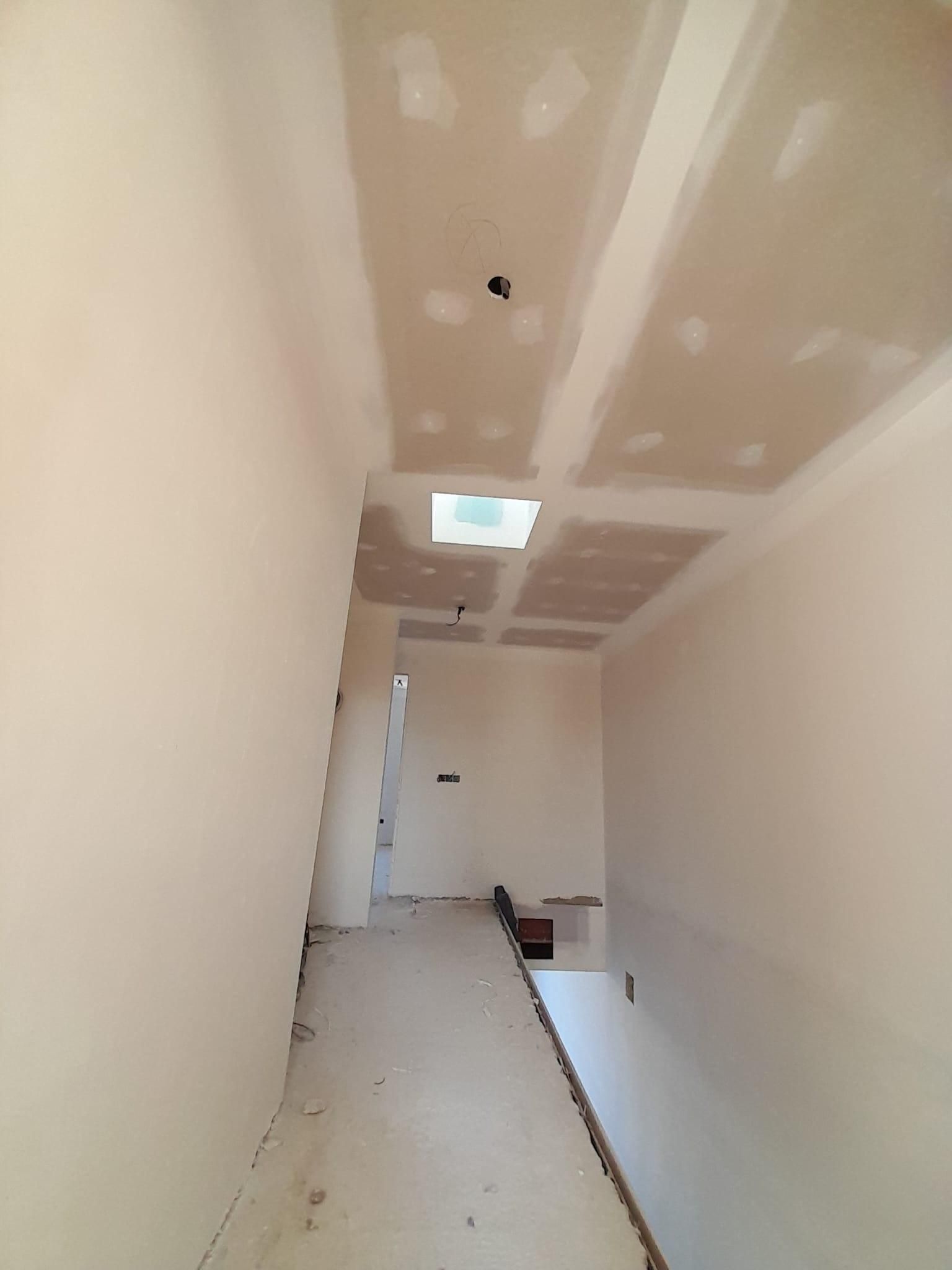 Un pasillo en construcción con paredes y techo de pladur sin terminar, una claraboya