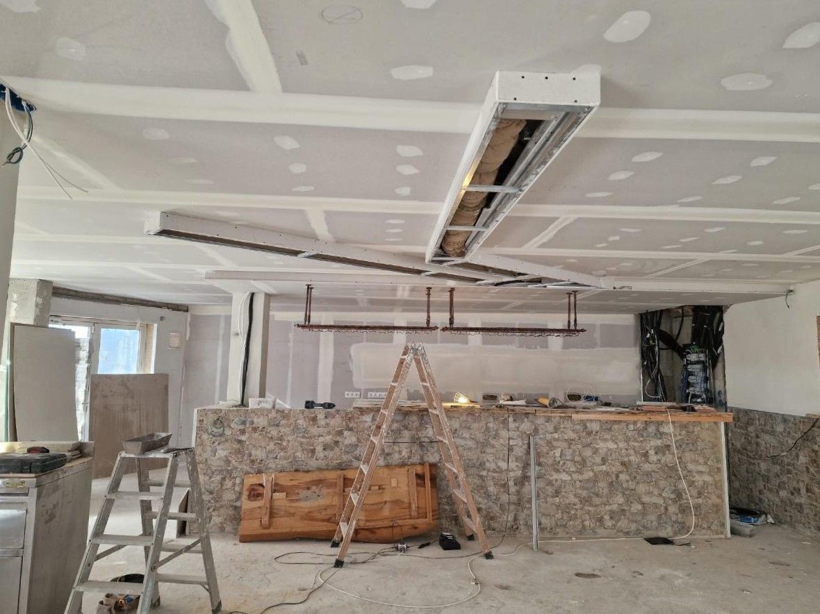 Una habitación interior en construcción presenta un techo parcialmente terminado con paneles de yeso y luminaria