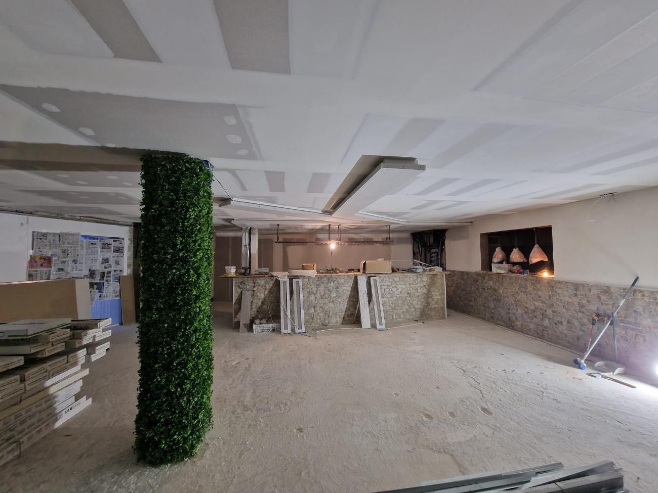 Una habitación en proceso de renovación con una columna de follaje artificial verde, techo de pladur