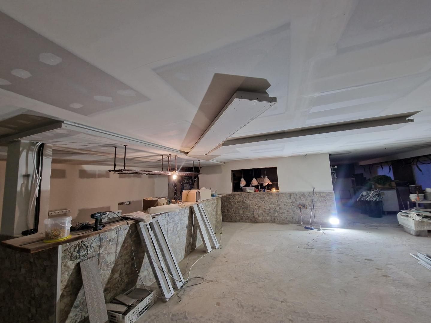 Una obra en construcción con paredes y techos de pladur sin terminar, materiales de estructura y suelo al descubierto.